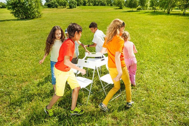 Kids run around chairs playing a game outside in summer period